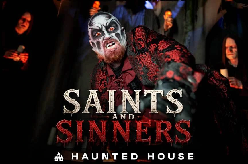 A terrifying, pale-faced vampire in a crimson and black velvet coat reaches out aggressively, surrounded by hooded figures holding candles in a dark chapel. The text reads "Saints and Sinners. Haunted House."